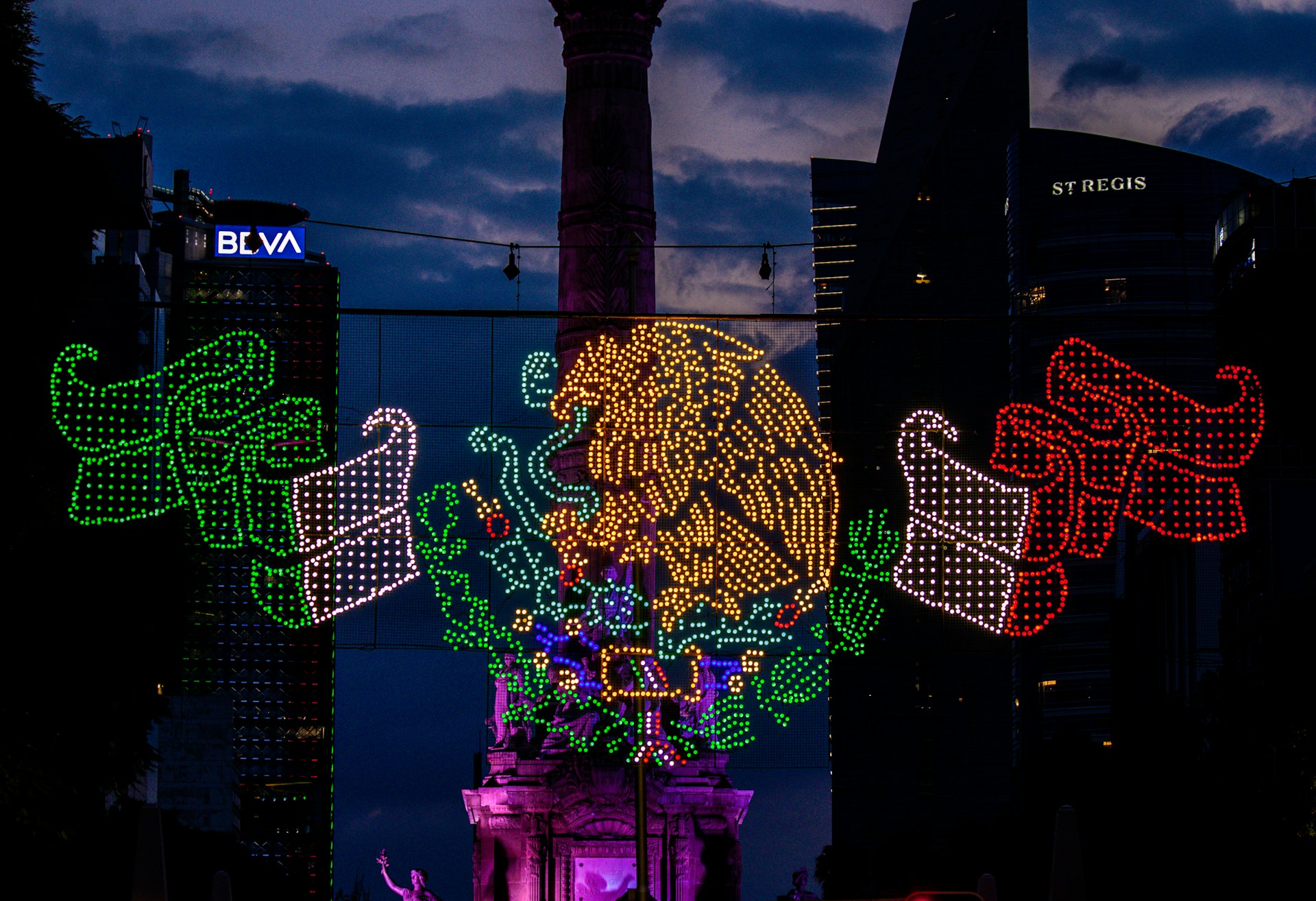 Iluminación del escudo nacional de México frente al Ángel de la Independencia en Ciudad de México